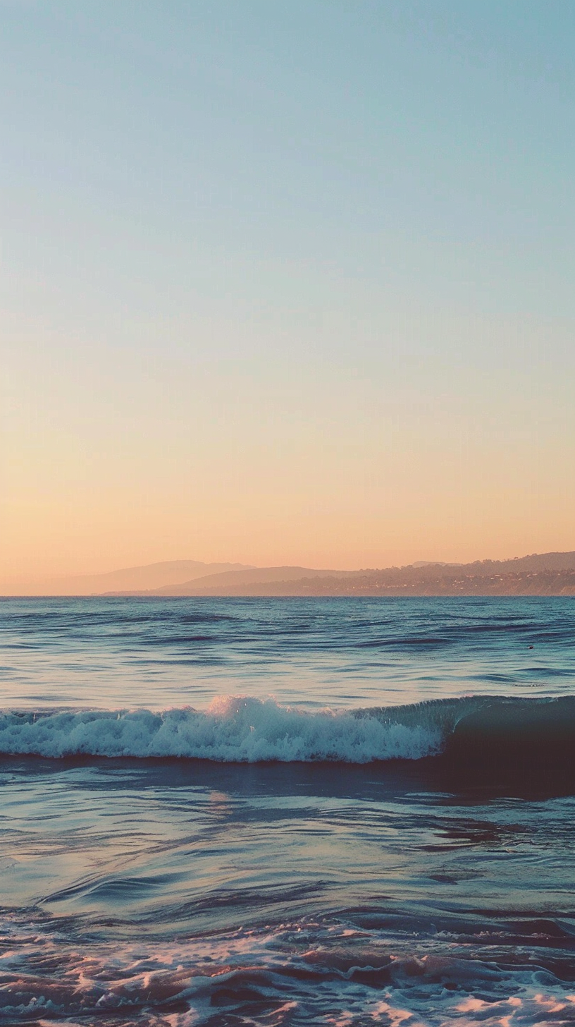 Waves lapping the beach, distant mountains light shadow blue sky, the beach scenery is quiet and beautiful.