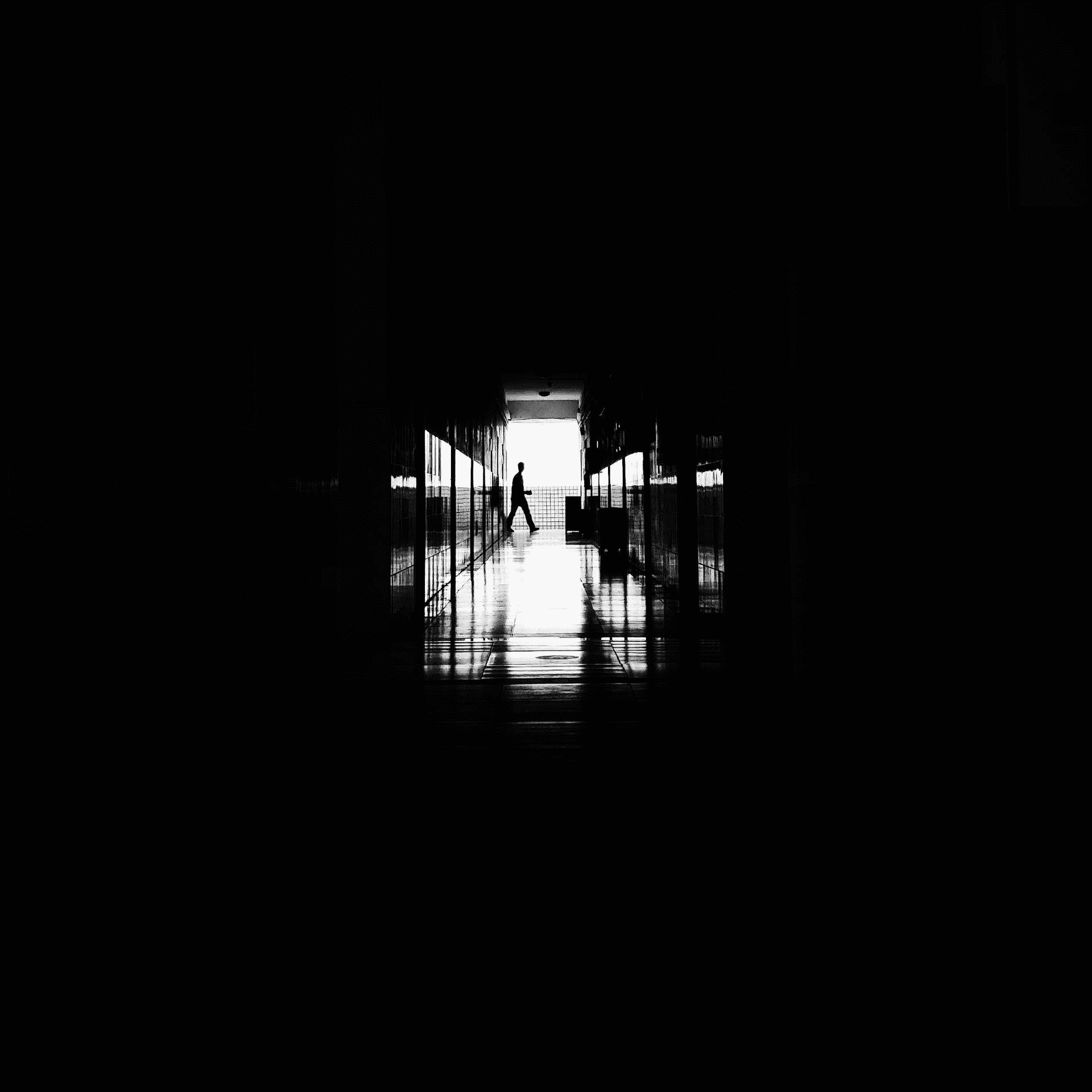 Shadows and a distant door in a dormitory corridor frame the subject, highlighting depth and focus.